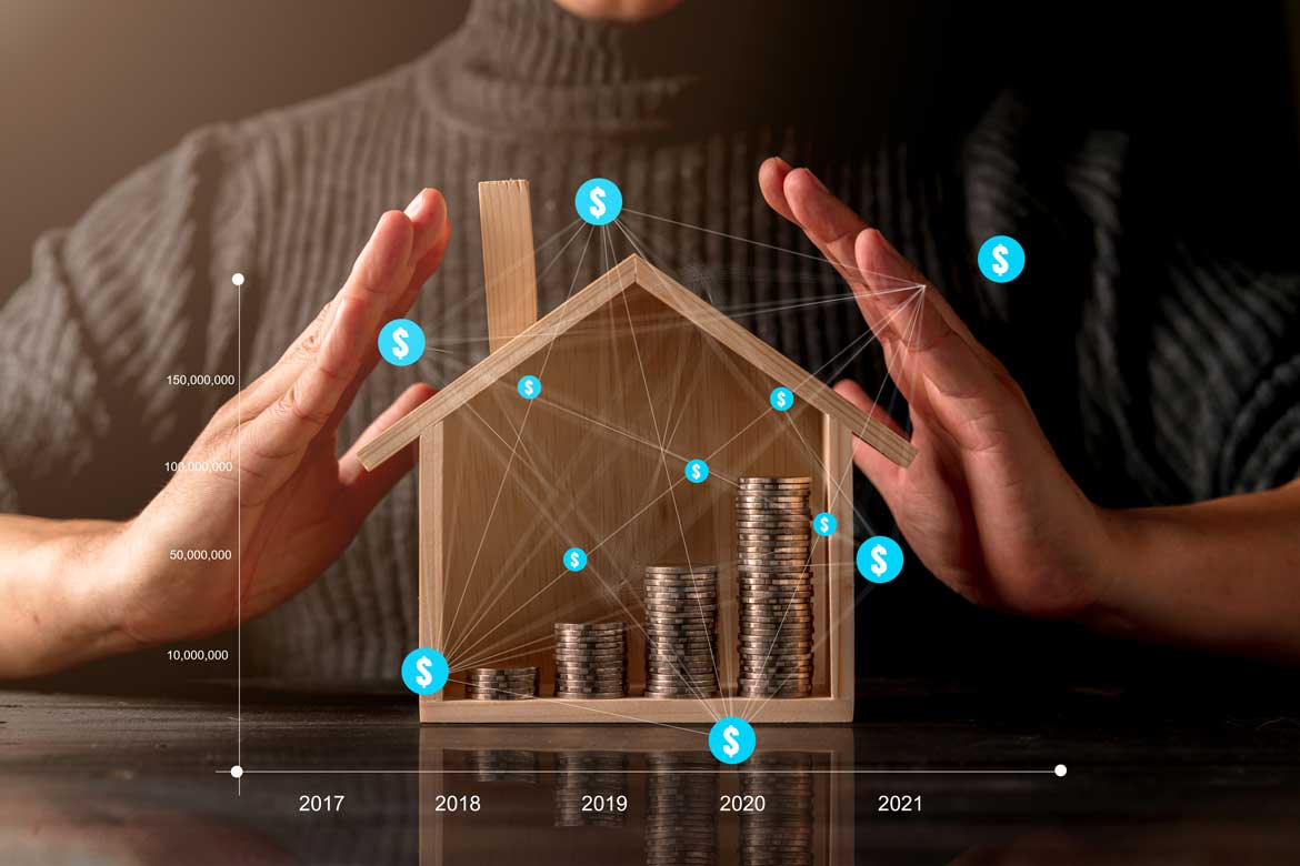 Person putting hands around wooden house with coins inside and graph overlay
