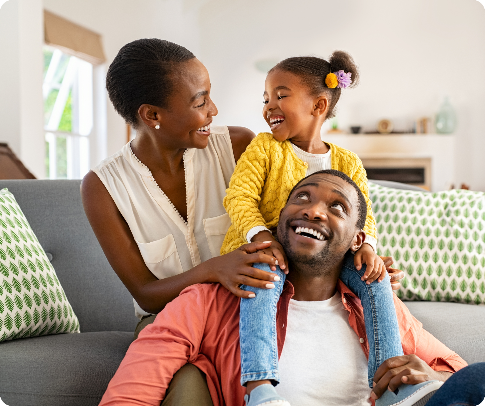 Woman sitting on a couch and smiling at a little girl on a sitting man's shoulders
