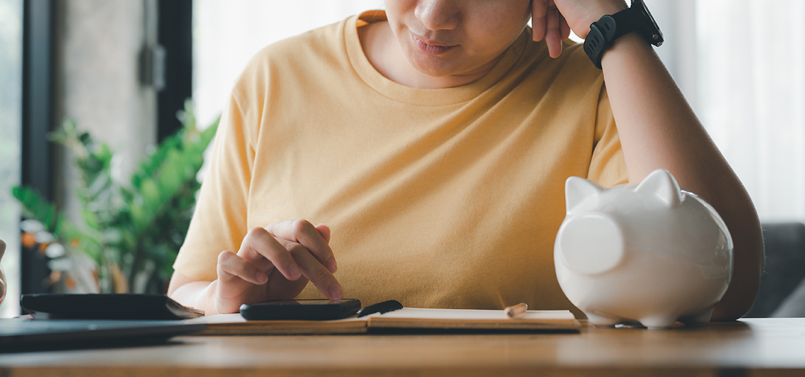 Woman using a calculator sitting at a table with a white porcelain piggy bank