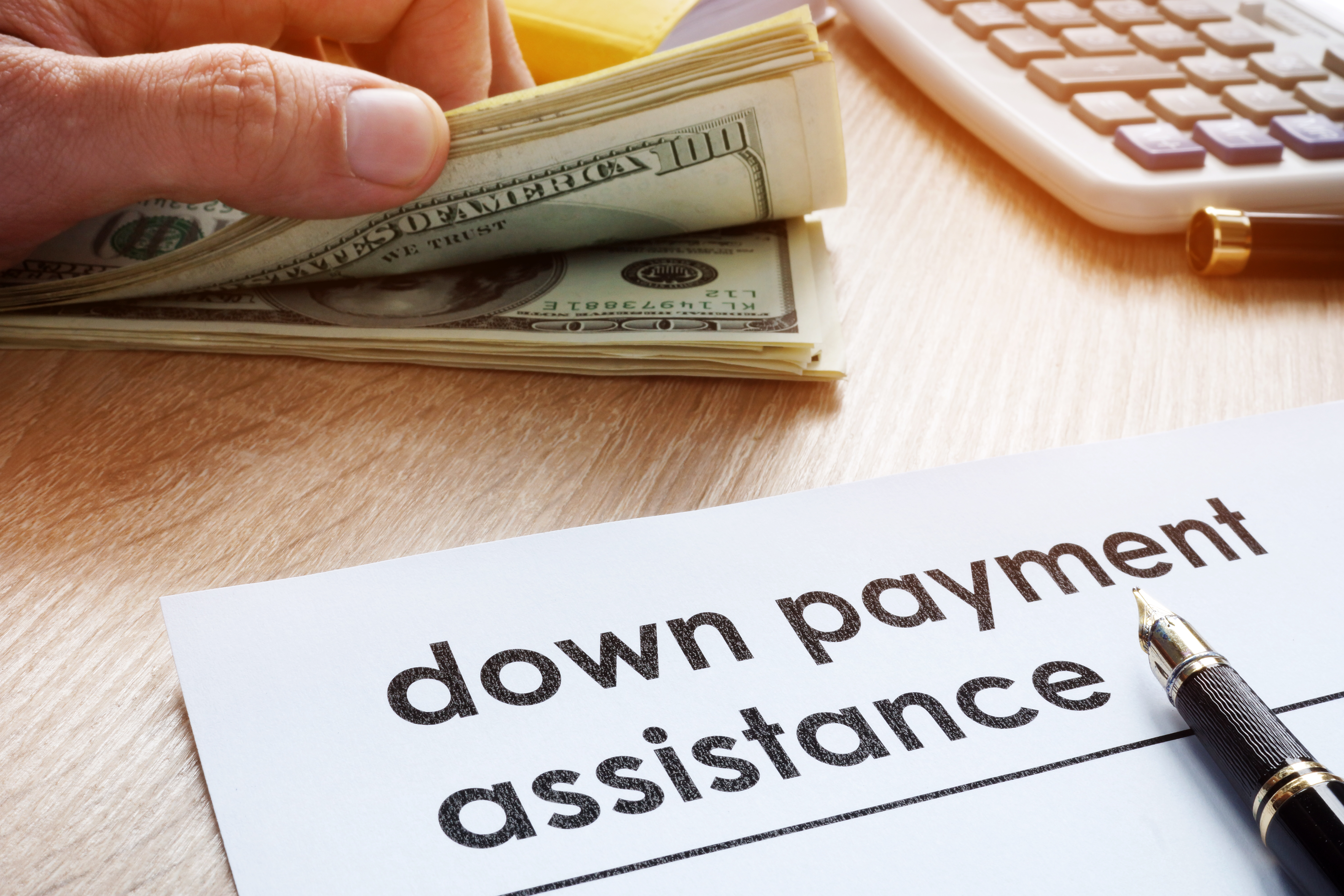 Hand holding money next to down payment assistance paper